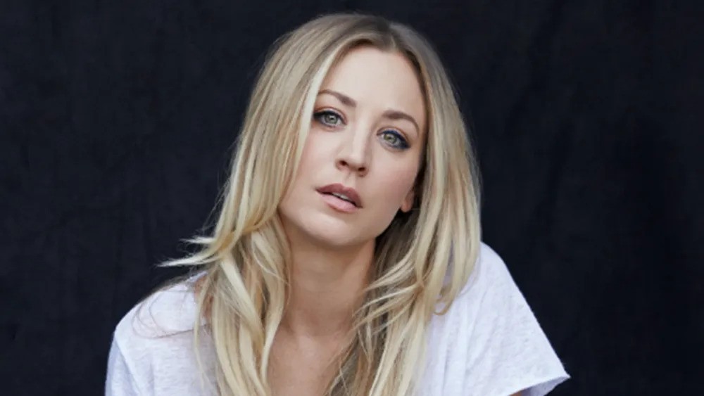 Kaley Cuoco with long hair is seated gracefully on a chair