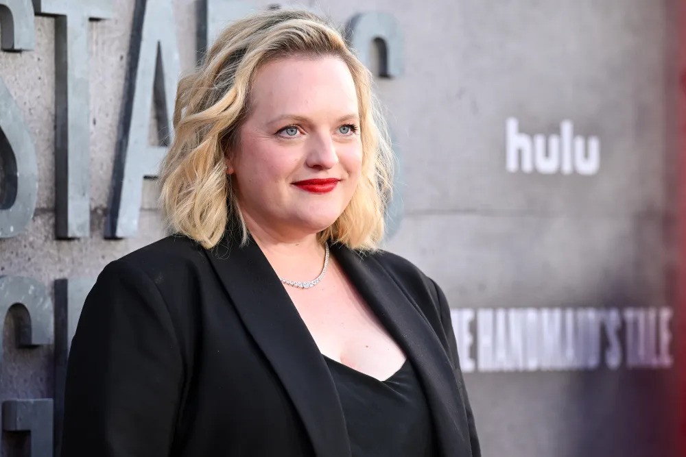 Elisabeth Moss in a black suit and red lipstick poses on the red carpet