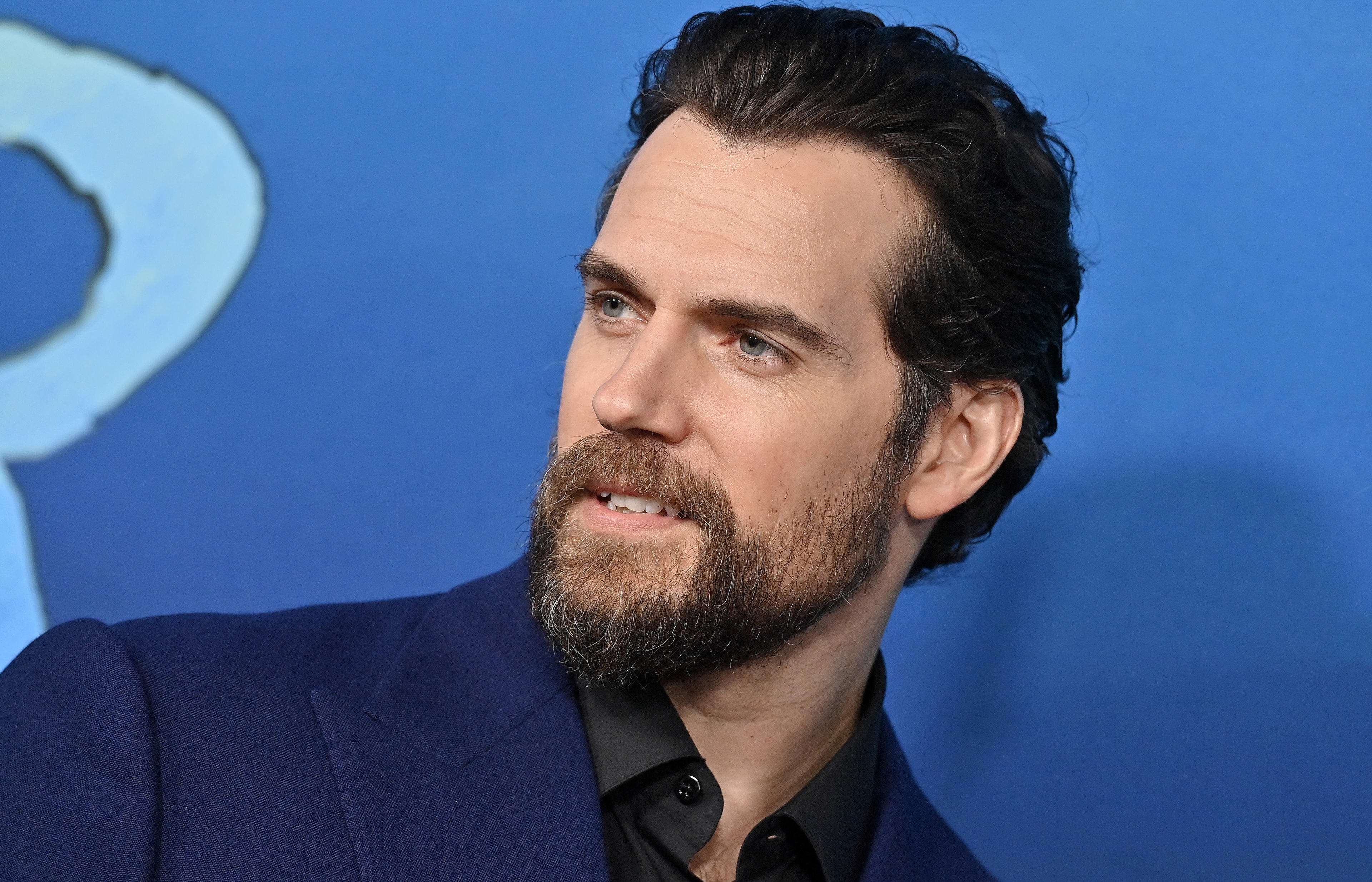 Henry Cavill in a suit gazes directly at the camera