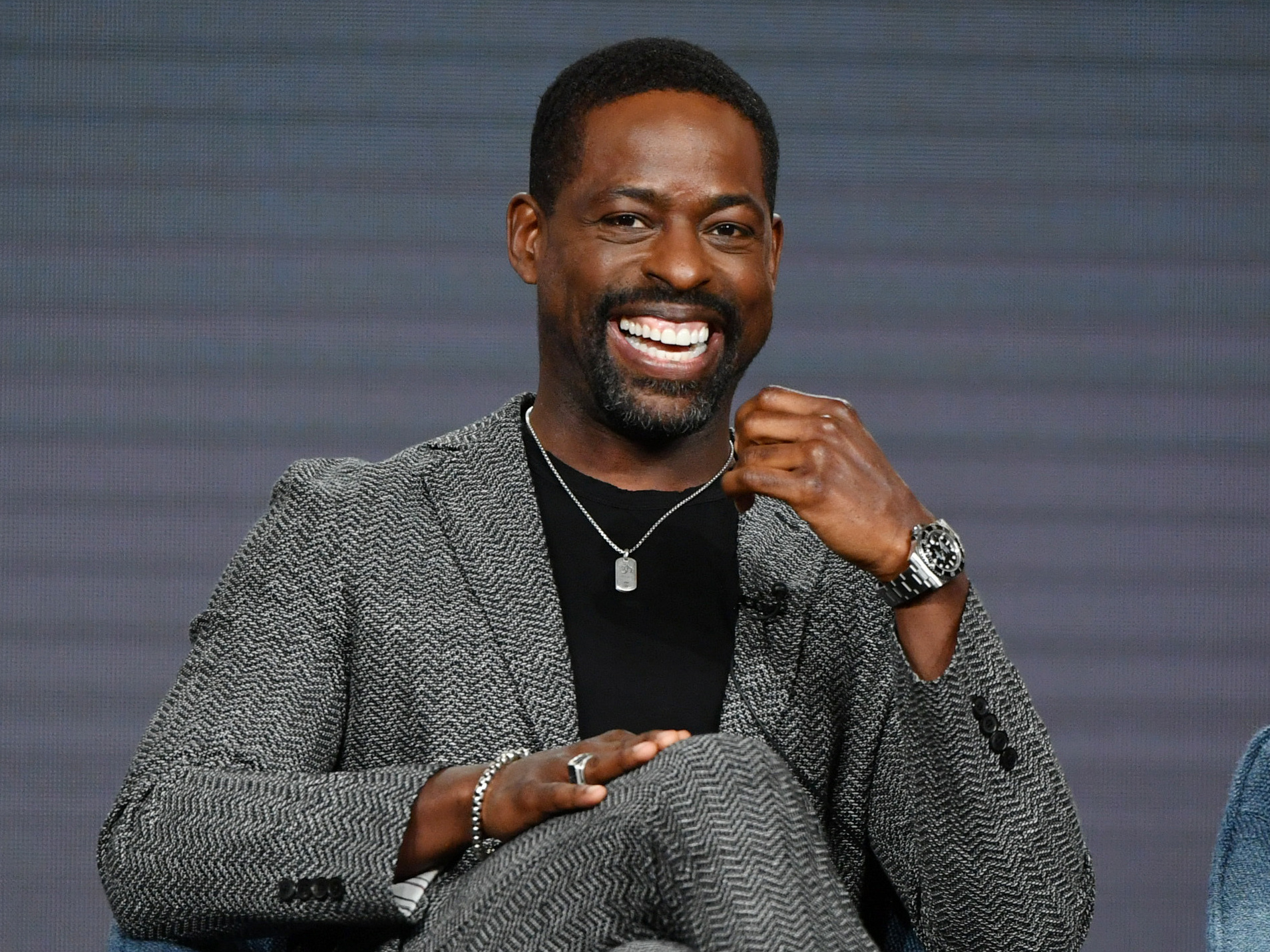 Sterling K. Brown in a suit sits on a chair